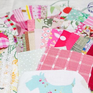 May include: A collection of pink, white, and green fabric scraps with a variety of patterns, including polka dots, stripes, and floral designs. The fabric scraps are arranged on a white surface and include a small, pink and white gingham fabric square.