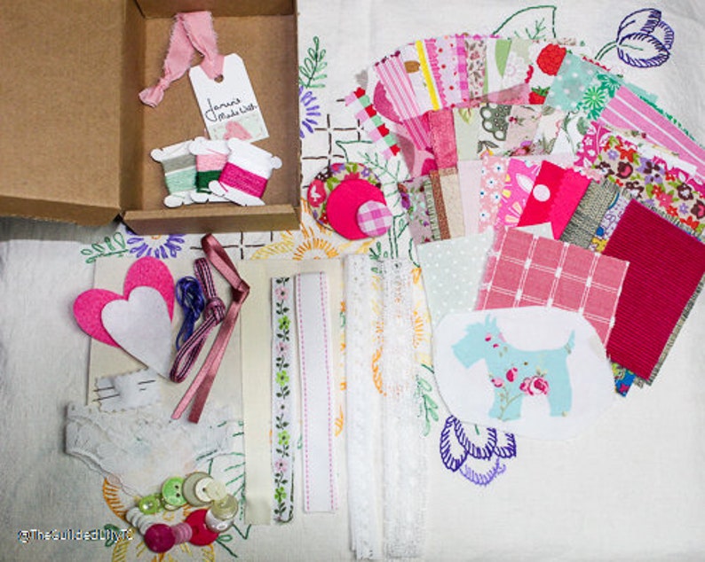 May include: A craft kit with a variety of fabrics, trims, and embellishments in pink, white, and green. The kit includes two felt hearts, a lace trim, a ribbon, and a small piece of fabric with a dog design. The kit also includes a tag that says "Jane Madish".