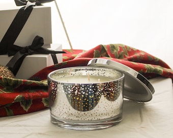 May include: A three-wick candle in a cylindrical glass jar with a reflective silver finish and a speckled pattern. The candle features a removable silver lid resting beside it, revealing white wax inside the container.