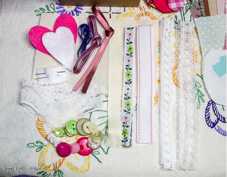 May include: A collection of craft supplies including white lace, pink ribbon, pink felt hearts, and green and white buttons.