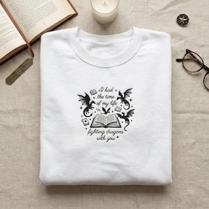 May include: White crew neck sweatshirt with a black graphic design featuring dragons, books, and the text "I had the time of my life fighting dragons with you."