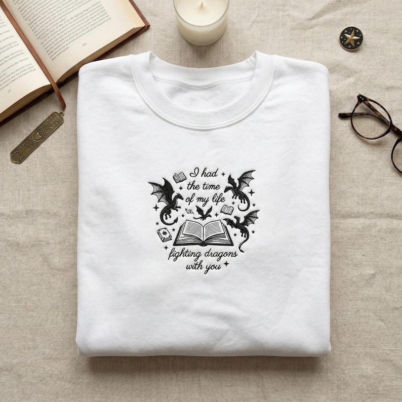 May include: White crew neck sweatshirt with a black graphic design featuring dragons, books, and the text "I had the time of my life fighting dragons with you."