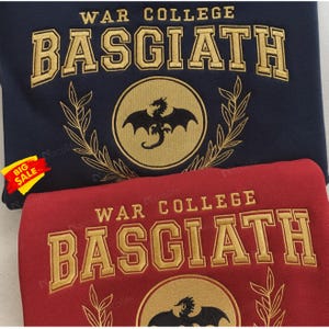 May include: Two sweatshirts, one navy blue and one red, with gold embroidered text and a dragon emblem. The navy blue sweatshirt has the text "WAR COLLEGE BASGIATH" and a dragon emblem inside a circle. The red sweatshirt has the same text and emblem.