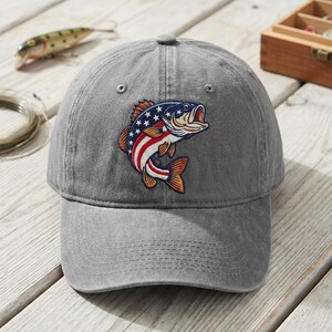 May include: A grey baseball cap featuring an embroidered graphic of a fish with a pattern of red and white stripes and white stars on a blue background. The cap has a curved brim, a button on top, and stitched eyelets for ventilation.