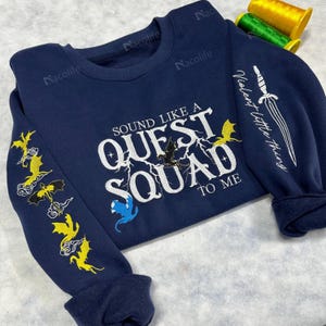 May include: A navy blue sweatshirt with the text "Sound Like A Quest Squad To Me" in white. The sleeves have embroidered yellow dragons and the right sleeve has the text "Violent Little Thing" in white.