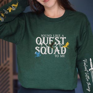 May include: Green long-sleeve sweatshirt with the text "Sound like a Quest Squad to me" and a graphic of dragons and a lightning bolt. The left sleeve has a graphic of flying dragons. The right sleeve has a graphic of a sword with the text "Violent Little Thing".