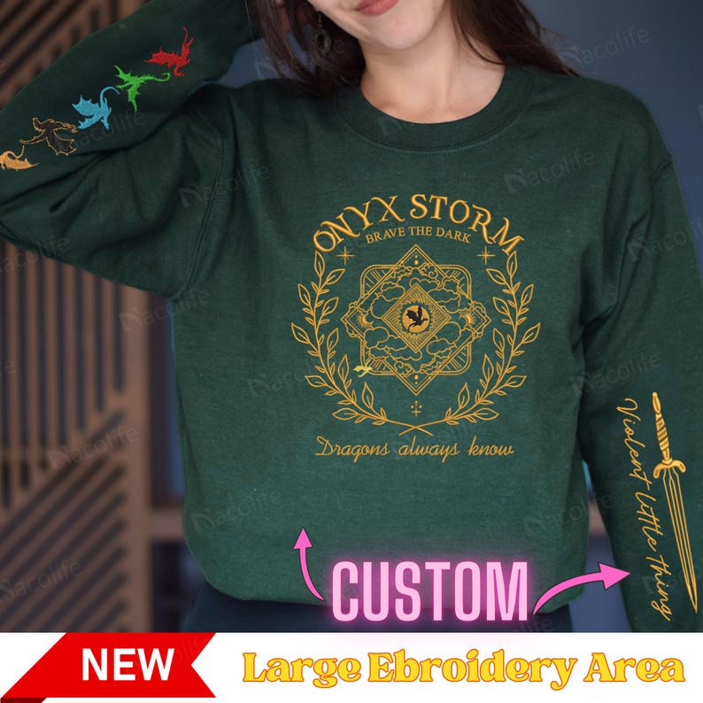 May include: Green long-sleeve sweatshirt with a gold embroidered design featuring a dragon, a wreath, and the text "ONYX STORM BRAVE THE DARK Dragons always know". The sweatshirt has a large embroidery area for customization.