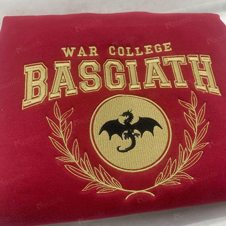 May include: A red sweatshirt with gold embroidered text and a circular emblem. The text reads "WAR COLLEGE BASGIATH". The emblem features a black dragon within a gold circle, surrounded by a gold laurel wreath.