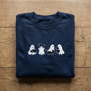May include: A navy blue crewneck sweatshirt featuring an embroidered design of four white ghosts interacting with small black cats. The embroidery depicts the ghosts holding, carrying, and playing with the cats in various positions across the chest.