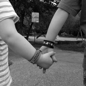 Puede incluir: Dos ni&ntilde;os se toman de la mano, uno lleva una camisa a rayas y el otro una camisa de color liso. Ambos ni&ntilde;os llevan pulseras.