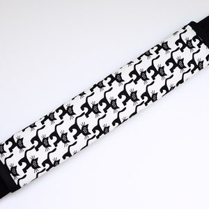 Könnte beinhalten: Ein weiß-schwarzes gemustertes Band mit einem sich wiederholenden Muster aus schwarzen Katzen. Das Band ist aus Stoff und hat einen schwarzen Rand.