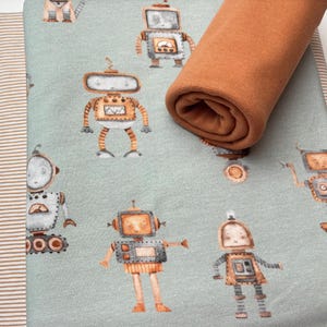 Könnte beinhalten: Ein hellblauer Stoff mit einem sich wiederholenden Muster von Robotern in verschiedenen Posen. Die Roboter sind braun, grau und weiß mit schwarzen Details. Der Stoff ist mit einem einfarbigen braunen Stoff kombiniert.