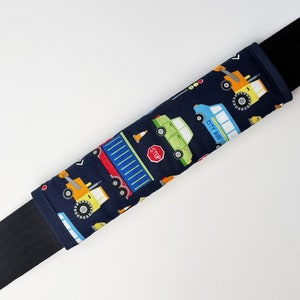 May include: A blue and black car seat belt cover with a pattern of various vehicles, including a city bus, a truck, and a construction vehicle. The pattern is on a dark blue background.