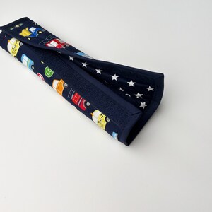 May include: A blue and white fabric car seat belt cover with a pattern of colorful cars and white stars.
