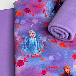 May include: Fabric featuring a colorful print with characters from a popular animated movie. The design includes images of two female characters, autumn leaves, and trees on a purple and blue background. A solid purple fabric is also visible.