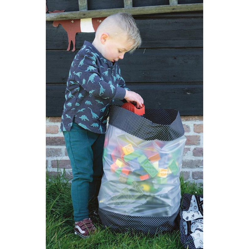 May include: A child is putting toys into a large black and white polka dot storage bag with a clear plastic lining. The bag is filled with colorful plastic building blocks.