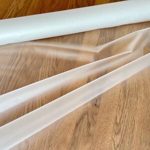 May include: A roll of clear plastic sheeting, unrolled and folded on a wooden surface.