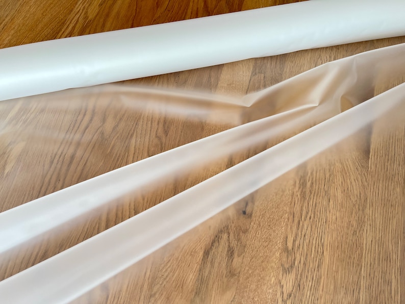 May include: A roll of clear plastic sheeting, unrolled and folded on a wooden surface.