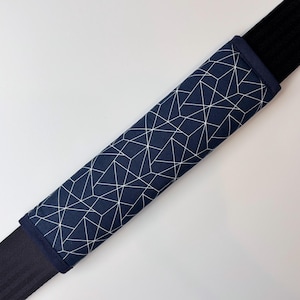 Op de afbeelding: Een donkerblauwe gordelpad met een wit geometrisch patroon. De pad is gemaakt van stof en heeft aan beide uiteinden een zwarte band.