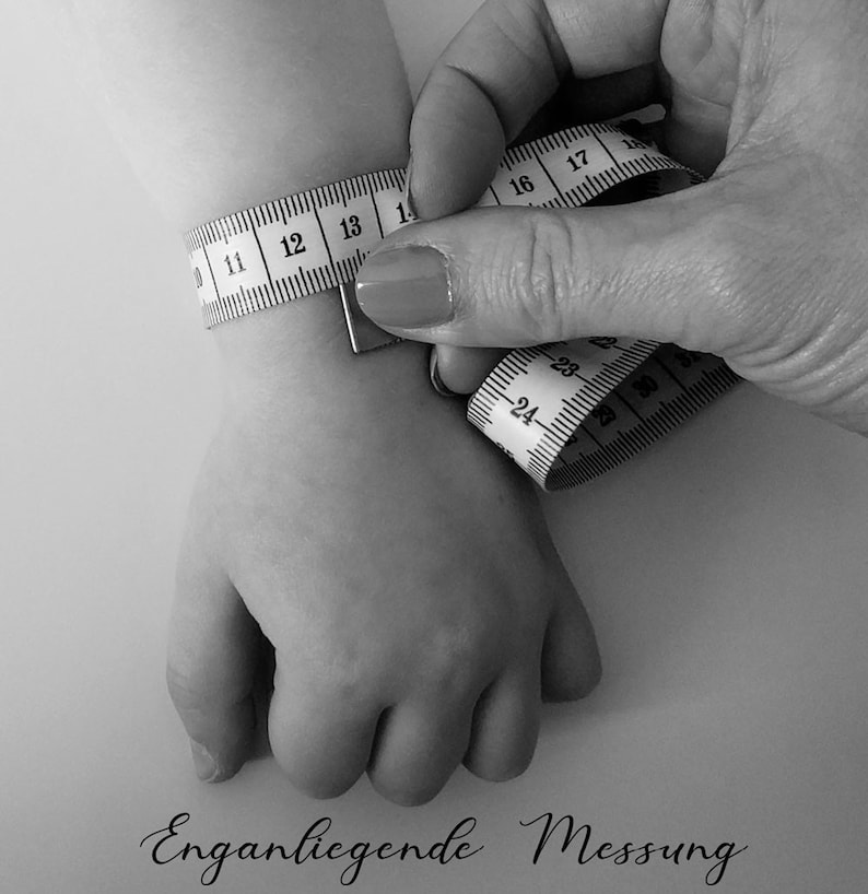 Puede incluir: Una cinta m&eacute;trica blanca est&aacute; envuelta alrededor de la mu&ntilde;eca de una persona. La cinta est&aacute; marcada con n&uacute;meros del 11 al 30. El texto "Enganliegende Messung" est&aacute; escrito debajo de la mu&ntilde;eca.