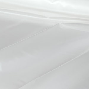 May include: A white, smooth, and shiny fabric with a subtle sheen. The fabric is folded in a way that creates a series of creases and folds.
