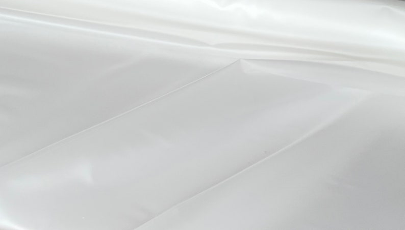 May include: A white, smooth, and shiny fabric with a subtle sheen. The fabric is folded in a way that creates a series of creases and folds.