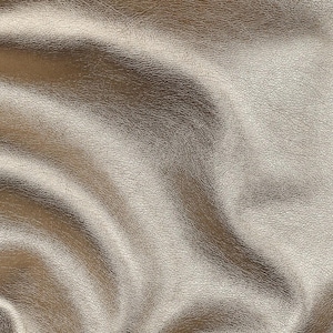 Op de afbeelding: Close-up van een metallic gouden leertextuur. Het oppervlak heeft een subtiele glans en een fijne, korrelige nerf. Het licht reflecteert op de plooien, waardoor highlights en schaduwen ontstaan. Dit materiaal is geschikt voor diverse knutselprojecten.