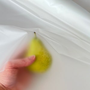May include: A yellow pear held in a hand, partially obscured by a white, translucent plastic sheet.