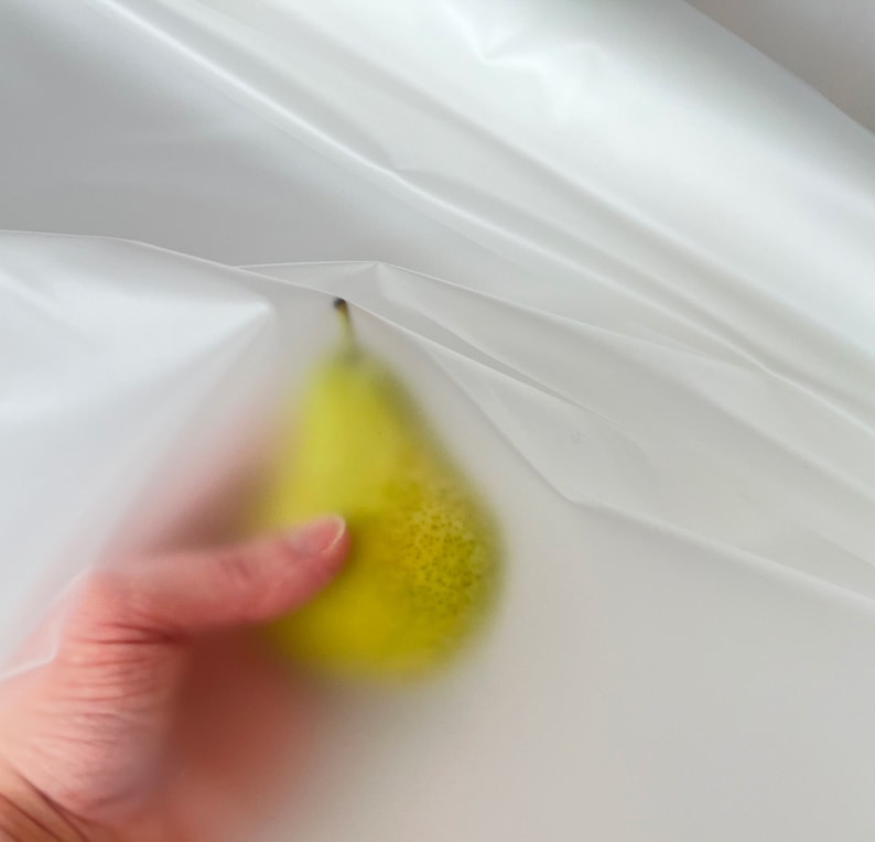 May include: A yellow pear held in a hand, partially obscured by a white, translucent plastic sheet.