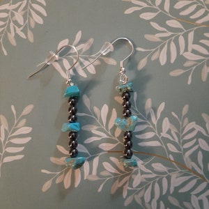 May include: A pair of dangle earrings with turquoise and black beads. The earrings are silver and have a hook closure.