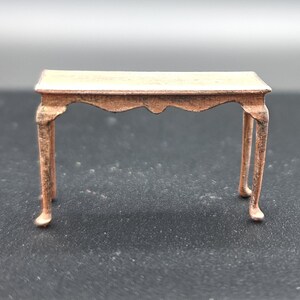 May include: A small, wooden table with a rectangular top and four legs. The table is a light brown color and has a slightly distressed finish.