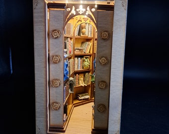 May include: A wooden miniature bookshelf with a light inside, showing a small library with books and a dragon figurine. The bookshelf has a decorative frame and is made of light wood.