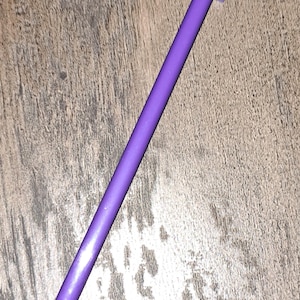 Pode incluir: Uma ferramenta de plástico roxo com uma ponta pontiaguda e uma cabeça plana retangular. A ferramenta é usada para aplicar cola ou outros adesivos.