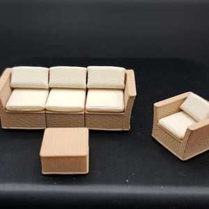 以下が含まれることがあります： ミニチュアパティオ家具セット。3人掛けソファ、アームチェア、正方形のコーヒーテーブルが含まれています。家具は、ライトブラウン色の織り籐のデザインで、クリーム色のクッションが付いています。