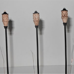 Puede incluir: Tres postes de luz de metal negro con pantallas de lámparas de estilo mimbre marrón. Cada poste de luz tiene una sola bombilla en la parte superior de la pantalla.