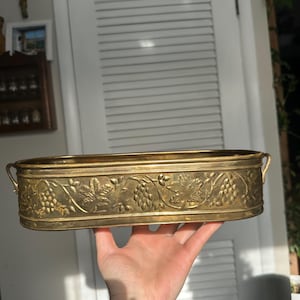 Puede incluir: Una taza de cerámica blanca con un asa negra y el texto "But first, coffee" en negro, con una fuente de estilo manuscrito. La taza está sobre una superficie blanca.