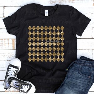 May include: Black t-shirt featuring a gold glitter diamond pattern. The shirt is laid flat on a white wooden background with a pair of black trainers and blue jeans.