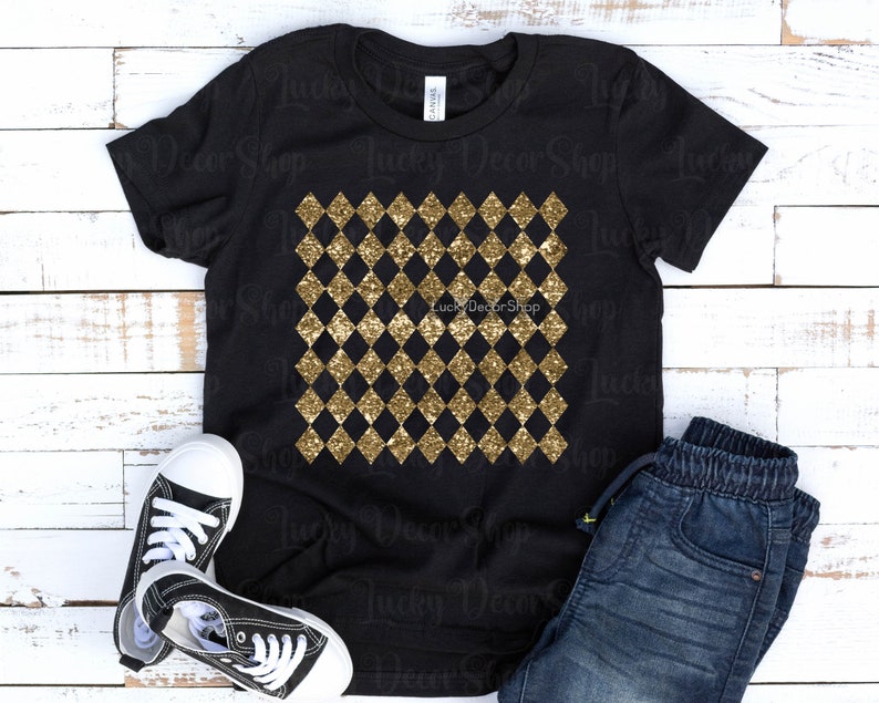 May include: Black t-shirt featuring a gold glitter diamond pattern. The shirt is laid flat on a white wooden background with a pair of black trainers and blue jeans.
