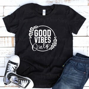 May include: Black t-shirt with a white circle graphic that says "Good Vibes Only" with a leopard print border.