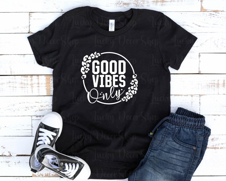 May include: Black t-shirt with a white circle graphic that says "Good Vibes Only" with a leopard print border.