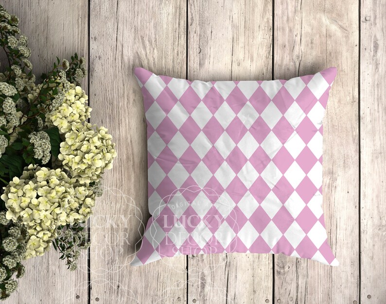 May include: A pink and white diamond patterned cushion. The cushion is on a light wood background.