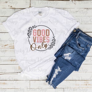 May include: White t-shirt with a gray circle and the text "GOOD VIBES ONLY" in pink and brown letters. The circle is surrounded by a leopard print design.