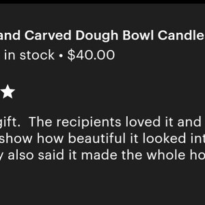 May include: A hand-carved wooden dough bowl candle featuring three lit wicks, positioned on a tray with a string of wooden beads. The text "Hand Carved Dough Bowl Candles" is visible, along with a five-star rating and a customer review about a gift.