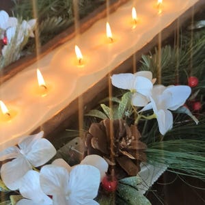 Pu&ograve; includere: Un centrotavola in legno con sette candele accese. Le candele sono poste in un lungo contenitore a forma di vasca. Decorato con fiori bianchi, aghi di pino, bacche rosse e una pigna.