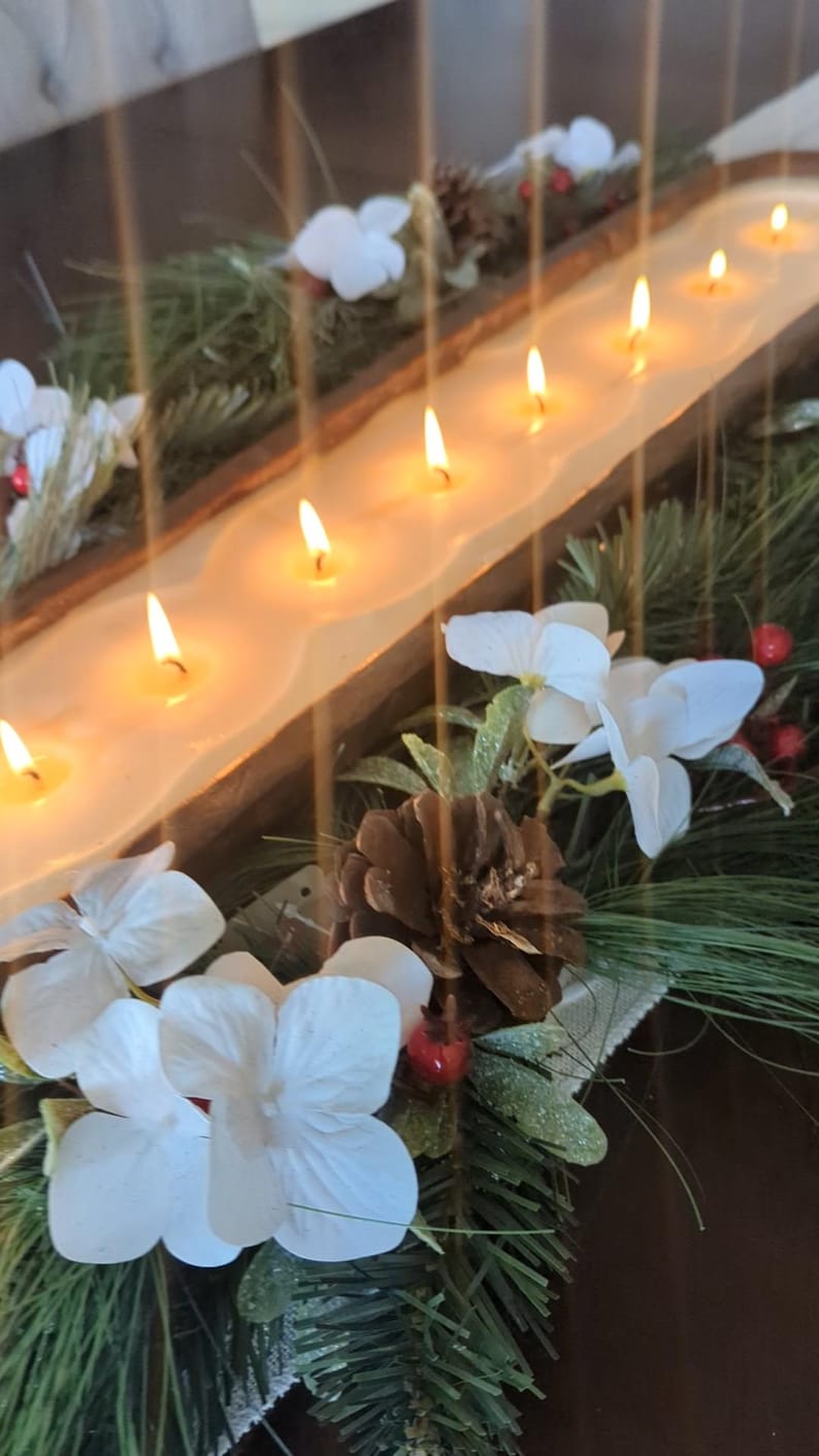 Pu&ograve; includere: Un centrotavola in legno con sette candele accese. Le candele sono poste in un lungo contenitore a forma di vasca. Decorato con fiori bianchi, aghi di pino, bacche rosse e una pigna.