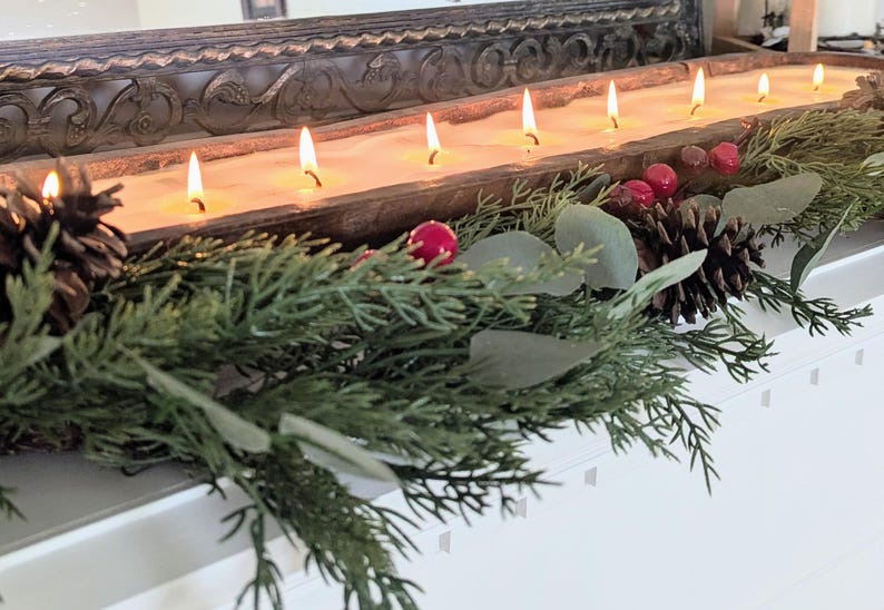 Pu&ograve; includere: Un lungo portacandele rettangolare in legno con pi&ugrave; stoppini accesi. Il portacandele &egrave; decorato con pigne, bacche rosse e rami sempreverdi. Le candele bruciano con un bagliore caldo e invitante, creando un'atmosfera festosa.