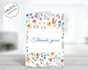 May include: A white thank you card with a floral border. The border features watercolor illustrations of pink, red, yellow, blue, and purple flowers. The text "Thank you" is written in blue ink inside a gold frame.