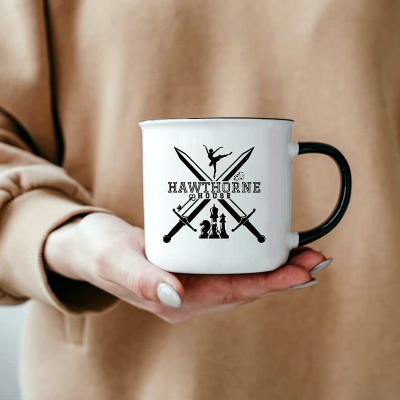 May include: White ceramic mug with a black rim and handle. The mug features a black graphic design with crossed swords, a ballerina, and chess pieces, with the text "HAWTHORNE HOUSE".