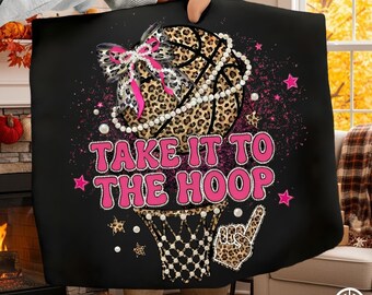 May include: Black blanket with a basketball design. The basketball has a leopard print pattern and is adorned with a pearl necklace and a pink bow. The text "TAKE IT TO THE HOOP" is in pink, with stars and a basketball net graphic.
