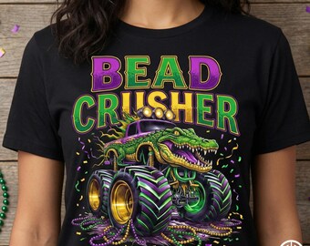 May include: Black t-shirt featuring a monster truck with a green alligator design. The text "BEAD CRUSHER" is in purple and green. The truck has gold rims and purple and green tires, with Mardi Gras beads.